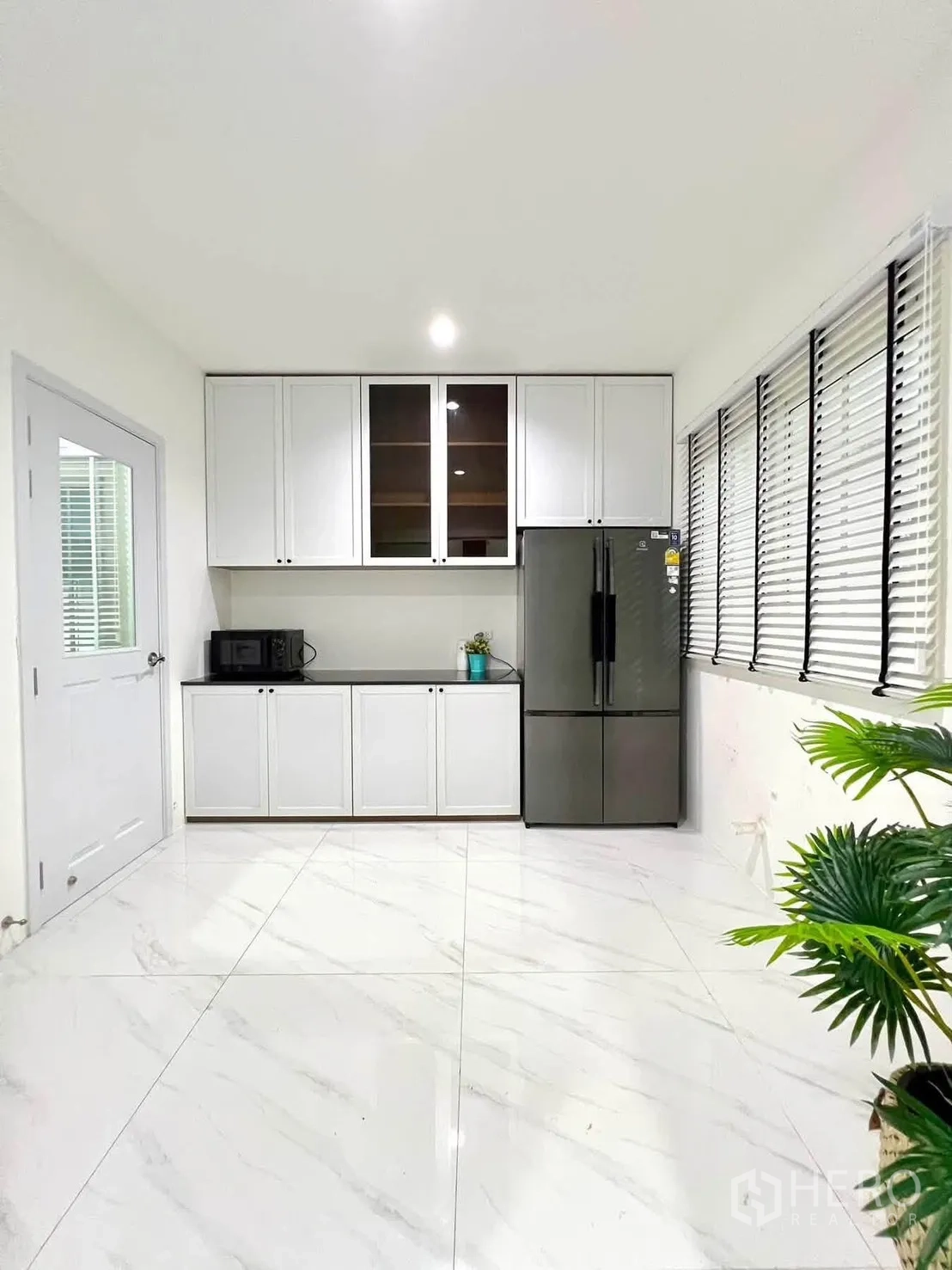 Detached House for rent in Bang Phli, Samut Prakan - Modern white kitchen with cabinets, black countertop, and a large refrigerator by long windows.