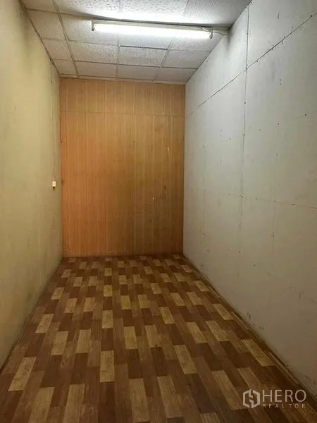 Shophouse for rent in Samphanthawong, Bangkok - Compact interior room with patterned vinyl flooring, wood panel end wall and tube light, ideal for storage.