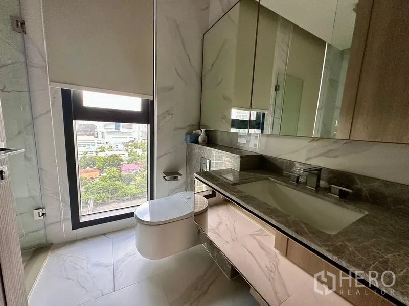 公寓 出租 - 卫浴洗手台为石质台面，镜柜充足收纳，窗外可见城市景观。