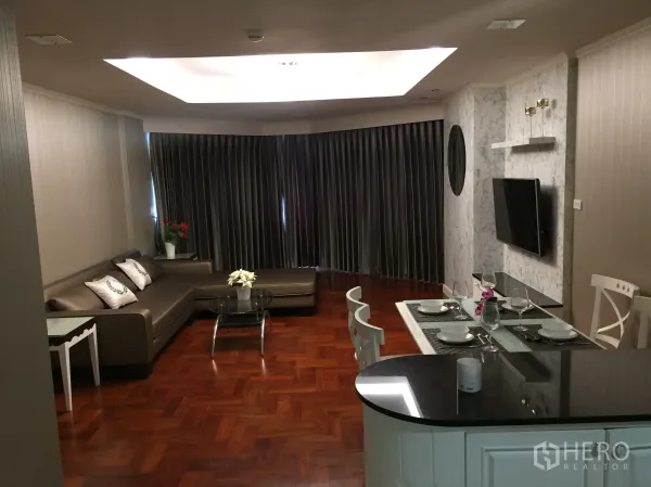 คอนโด ให้เช่าในKhlong Toei, Bangkok - โซนรับแขกและทานอาหารแบบโอเพนแพลน โซฟาเข้ามุมรูปตัว L ทีวีติดผนัง เคาน์เตอร์บาร์ และไฟดาวน์ไลท์