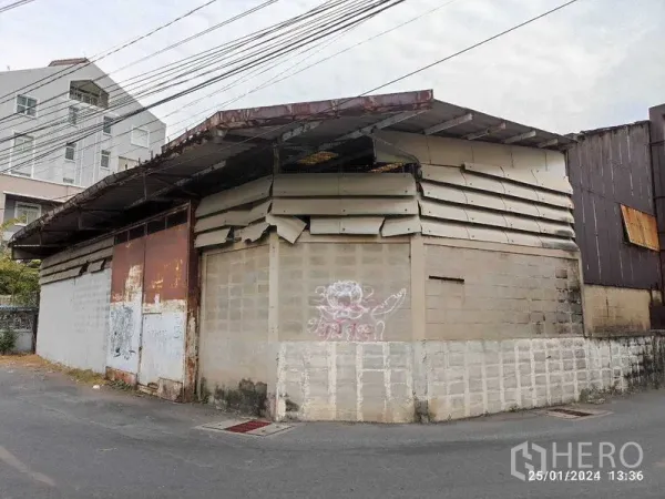 คลังสินค้า ให้เช่าในWatthana, Bangkok - ทัศนียภาพหน้าโกดังเก่าพร้อมประตูเหล็กขึ้นสนิมและอาคารพักอาศัยใกล้เคียง