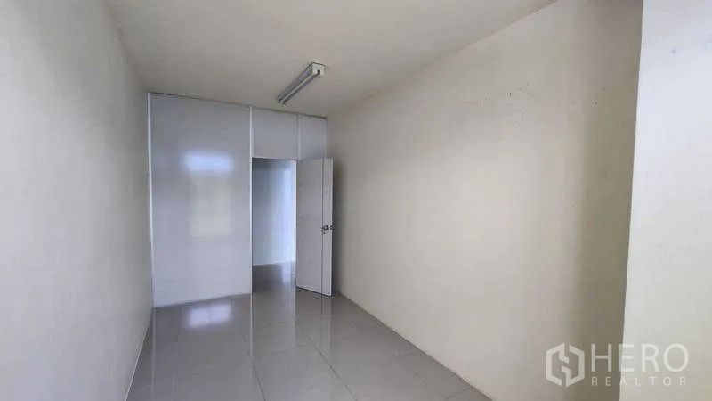 Factory for rent in Samut Sakhon - Long tiled room with door and built-in wall panels for storage.