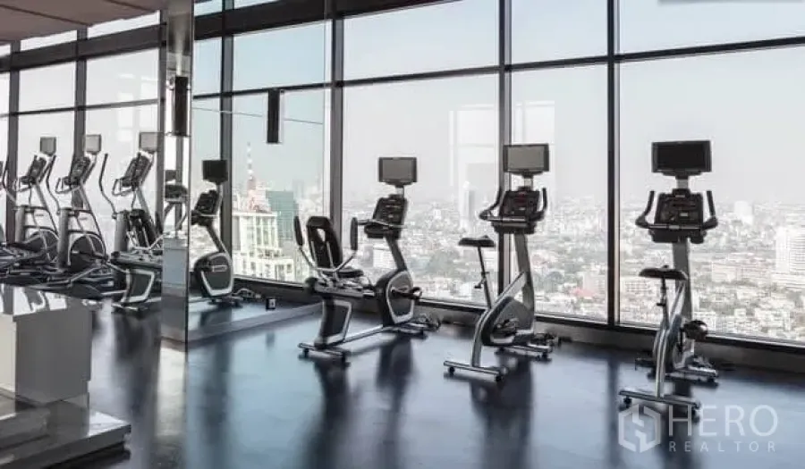 Condominium for rent in Khlong Toei, Bangkok - Skyline-view fitness center with treadmills and bikes beside floor-to-ceiling windows.