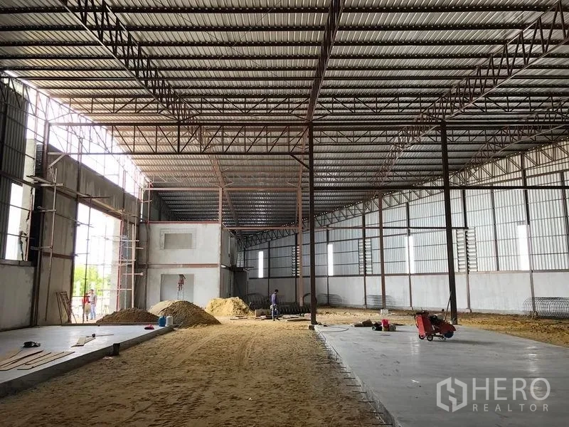 Warehouse for rent or sale in Sai Noi, Nonthaburi - Spacious warehouse interior with high metal trusses, large loading door openings, and unfinished floor.