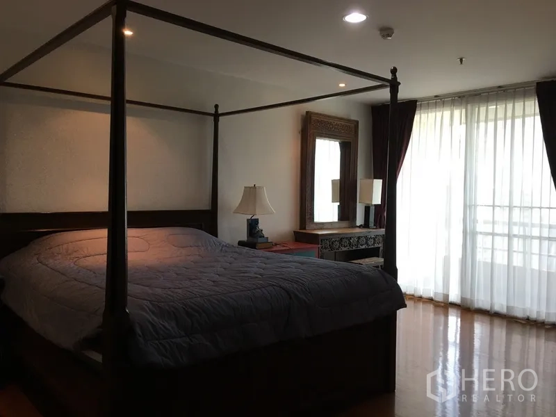 Condominium for rent in Pathum Wan, Bangkok - Spacious master bedroom with four-poster bed and floor-to-ceiling sheer curtains leading to a balcony.