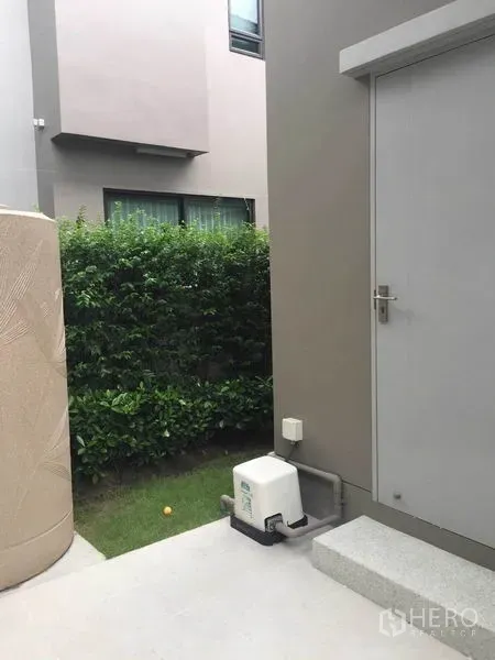 Detached House for sale in Pak Kret, Nonthaburi - Side service door with step, utility pump and hedge-lined yard