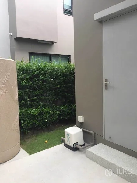 Detached House for sale in Pak Kret, Nonthaburi - Side service door with step, utility pump and hedge-lined yard