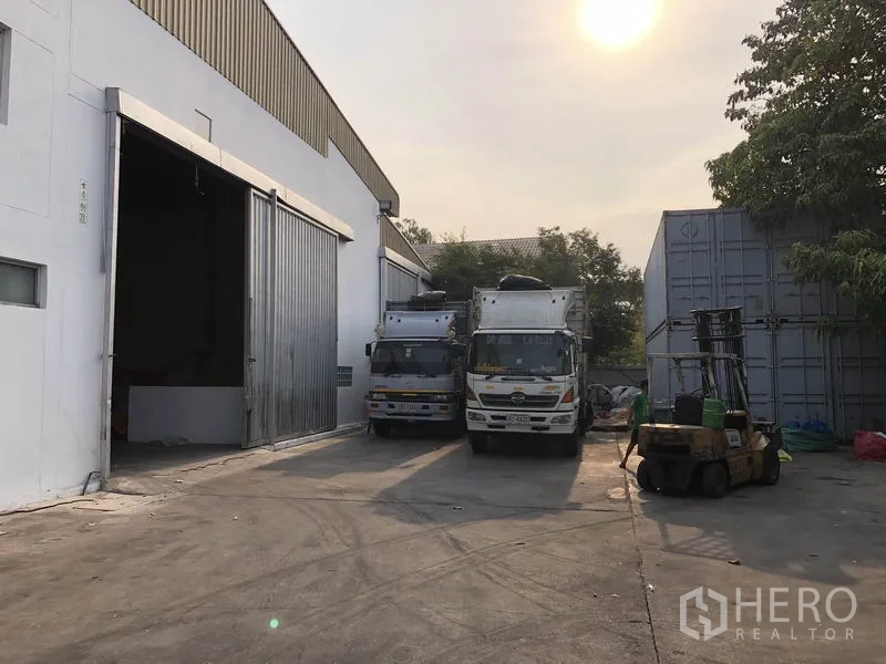 工厂 出租在Bang Bua Thong, Nonthaburi - 厂房侧装卸场，集装箱卡车与叉车通道，夕阳光线。