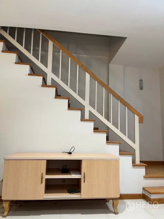 Townhouse for rent in Bang Kho Laem, Bangkok - Wooden staircase detail with light-wood TV console underneath.