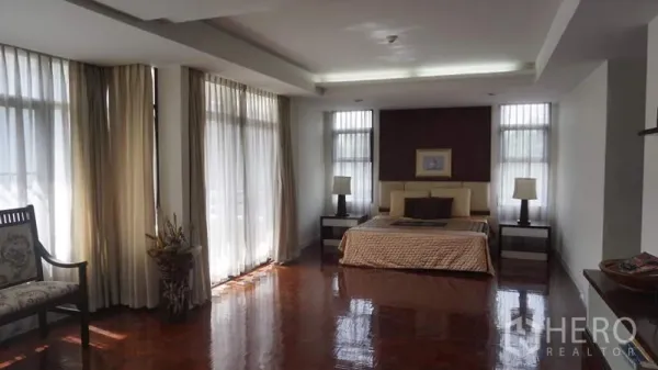 房间 出租在Khlong Toei, Bangkok - 宽敞主卧，配有特大床、床头柜、落地窗帘与光洁的木地板。