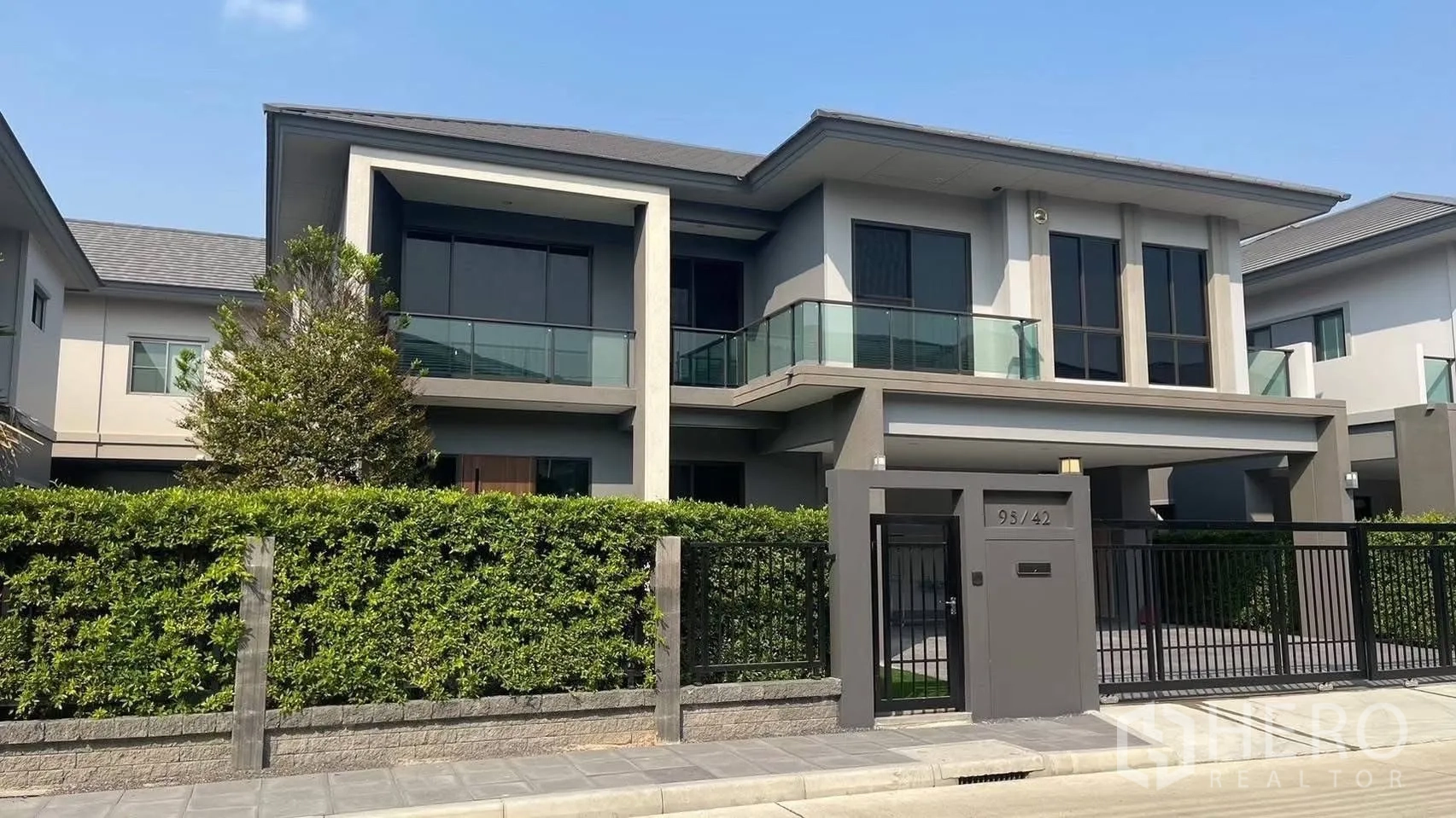 Detached House for rent in Prawet, Bangkok - Street view of the two-storey detached house with gated entrance and hedge.