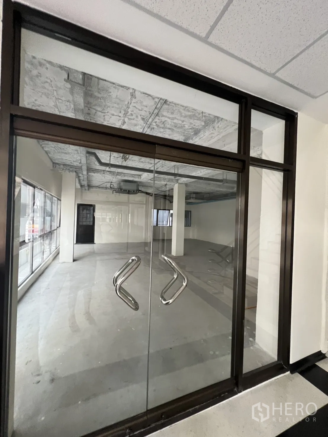 零售空间 出租在Watthana, Bangkok - 带双开玻璃门的商铺入口，可见通透开间与未完成天花。