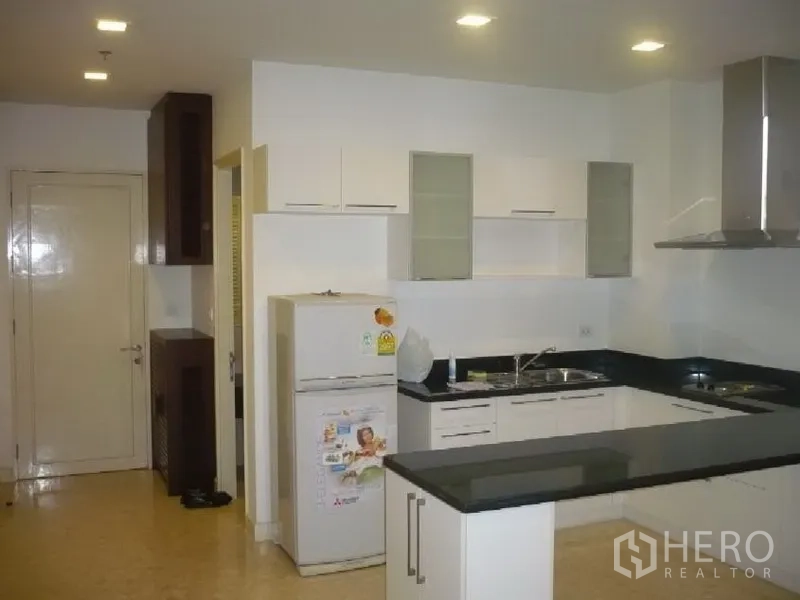 公寓 出租在Khlong Toei, Bangkok - Ekkamai公寓的L形白色厨房，黑色台面、抽油烟机与冰箱。