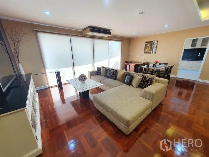 Condominium for rent in Watthana, Bangkok - Bright lounge with large windows, sectional sofa, and adjoining dining area.