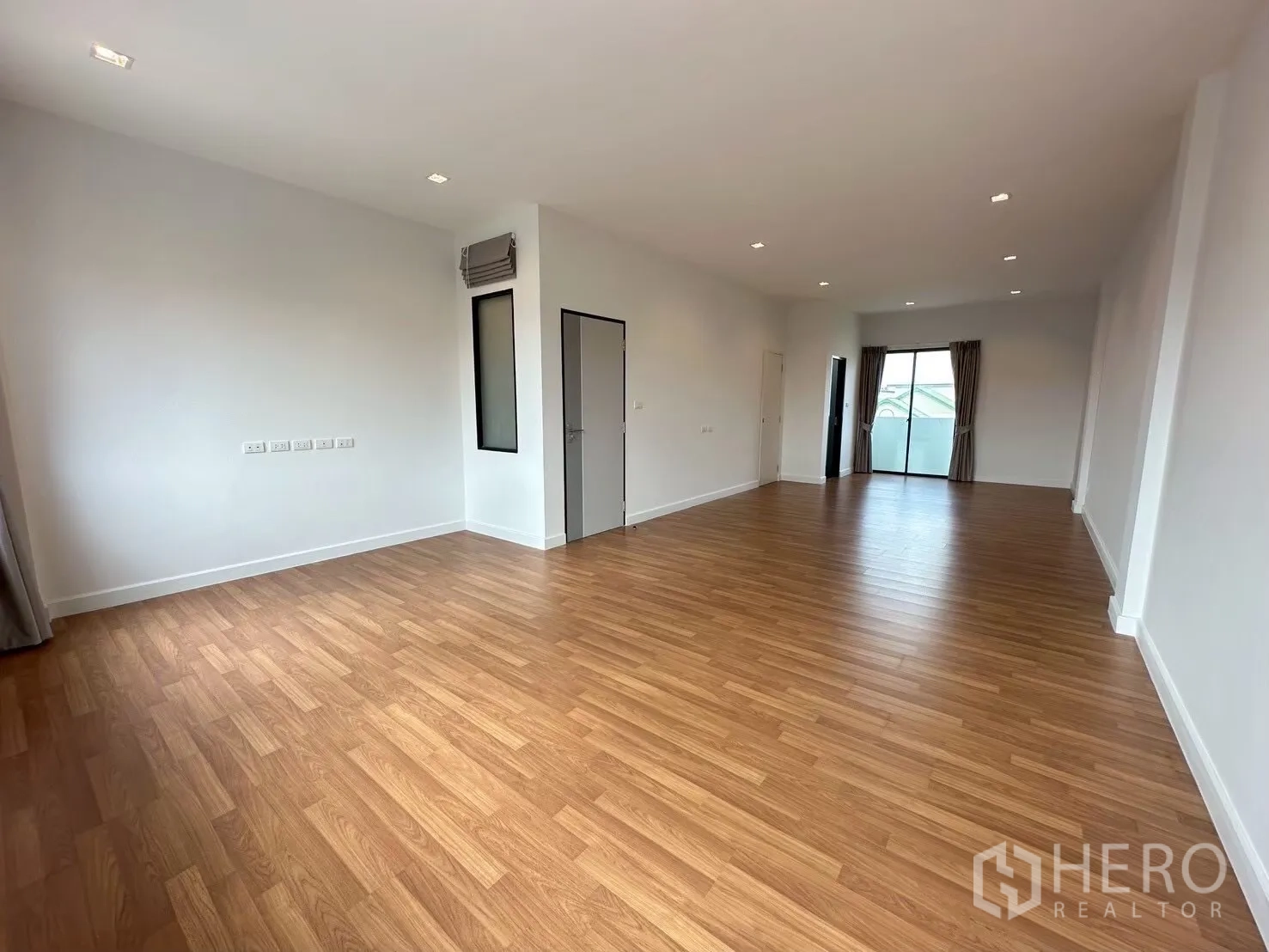 สำนักงานที่บ้าน for rent in Lat Phrao, Bangkok - พื้นที่อเนกประสงค์ยาว พื้นไม้ และประตูกระจกสู่ระเบียงทั้งสองด้าน.