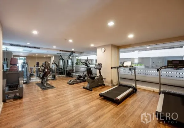 Condominium for sale in Watthana, Bangkok - Fitness room with treadmills, weight machines and wooden flooring overlooking the courtyard.