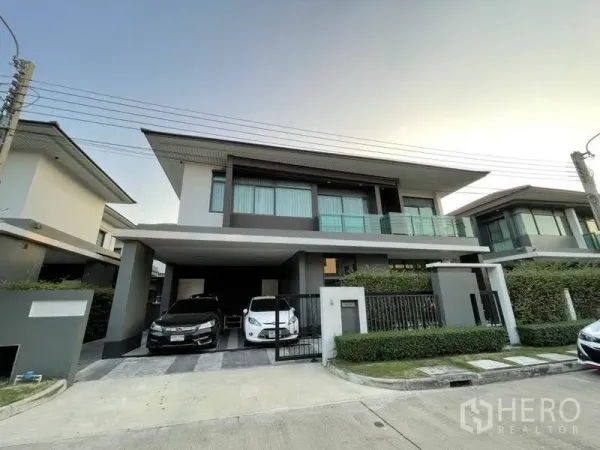 Detached House for rent in Bang Kapi, Bangkok - Modern two-storey detached house with covered double carport, glass balcony, and gated hedge-lined front yard in a Setthasiri Krungthep Kreetha compound, Bang Kapi.