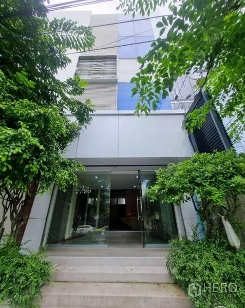 店屋 出租在Watthana, Bangkok - 通罗区域店屋外观，玻璃入口与绿树环绕的现代立面。