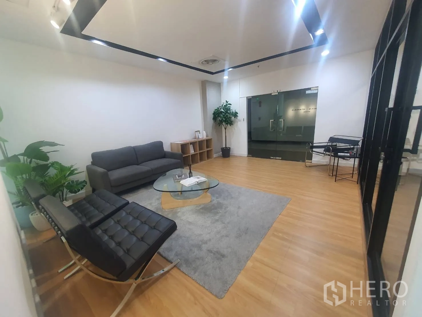 办公室 for rent in Watthana, Bangkok - 现代接待区，配灰色沙发、黑色椅子、玻璃茶几、木地板与玻璃门。