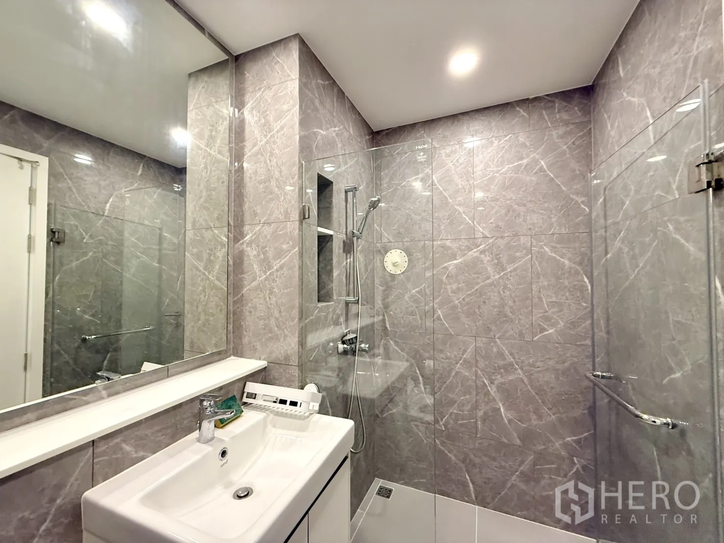 Condominium for sale in Chatuchak, Bangkok - Glass-enclosed shower and vanity inside a stone-tiled bathroom.