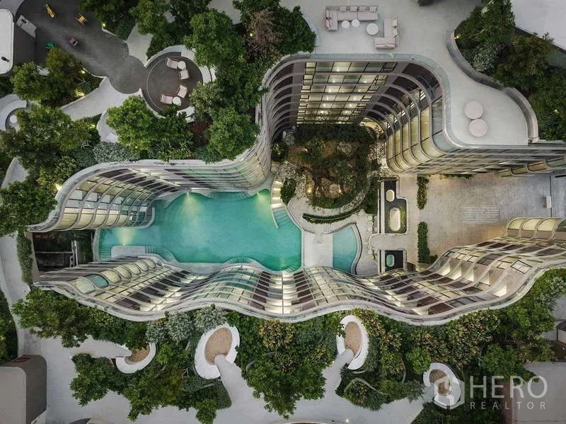คอนโด ให้เช่า - มุมมองมุมสูงของอาคารโค้งล้อมรอบสระว่ายน้ำสไตล์รีสอร์ทและสวนสีเขียวของโครงการ