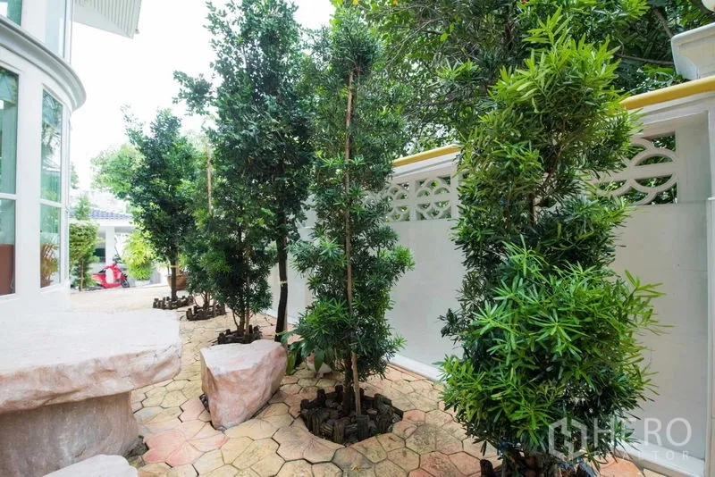 Detached House for rent or sale in Bang Kapi, Bangkok - Shaded garden walkway with tall trees along a white privacy wall.
