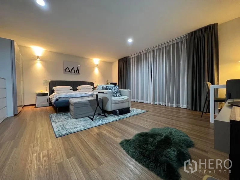 Townhouse for sale in Suan Luang, Bangkok - Spacious master bedroom with wood flooring, king bed, lounge seating and floor‑to‑ceiling curtains in a Suan Luang townhouse.