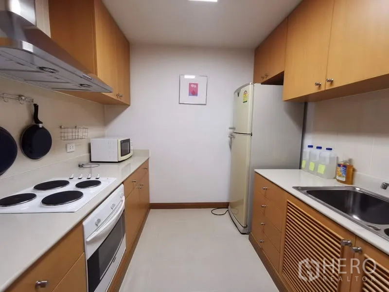 公寓 出租在Pathum Wan, Bangkok - 走廊式厨房，配电炉、烤箱、油烟机、微波炉、冰箱与木质橱柜。