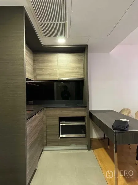 Condominium for sale in Pathum Wan, Bangkok - Compact modern kitchen with dark wood cabinets, built-in appliances and an adjacent dining table.