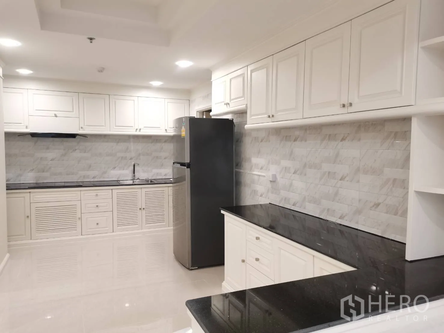Condominium for rent in Watthana, Bangkok - Bright kitchen with white cabinetry, marble tile backsplash, and black stone countertops plus fridge.