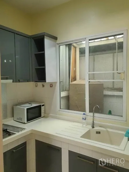 Townhouse for rent in Wang Thonglang, Bangkok - Compact fitted kitchen with cabinets, sink, stove and window.