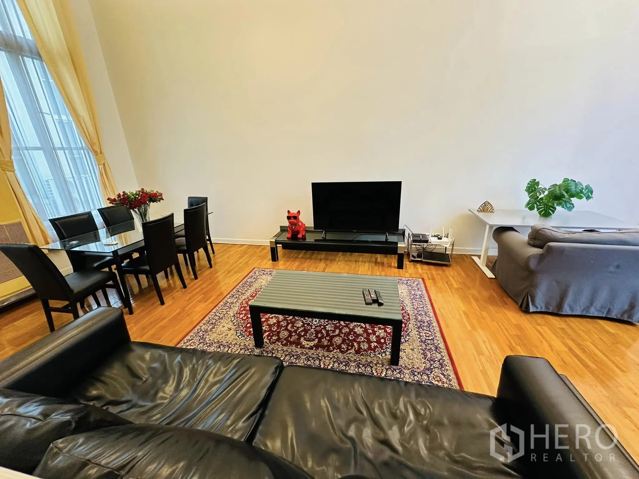 Townhouse for rent in Watthana, Bangkok - Spacious living room with TV console, sofas, glass dining set, patterned rug and wood flooring.