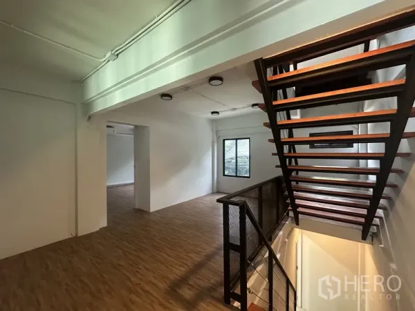 Home Office for rent or sale in Khlong Toei, Bangkok - Open workspace beside a metal‑and‑wood staircase and window, featuring warm flooring.