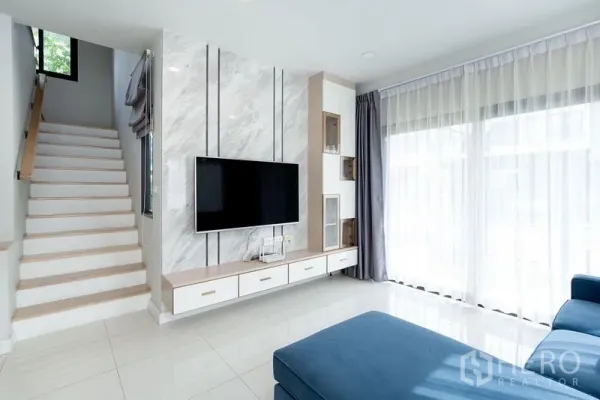 独立式住宅 出租在Bang Phli, Samut Prakan - 明亮客厅，带大理石风电视墙、楼梯与落地窗帘。