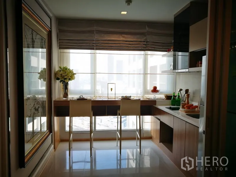 公寓 出租在Sathon, Bangkok - 明亮厨房，窗边长吧台配两张高脚椅与简洁橱柜。