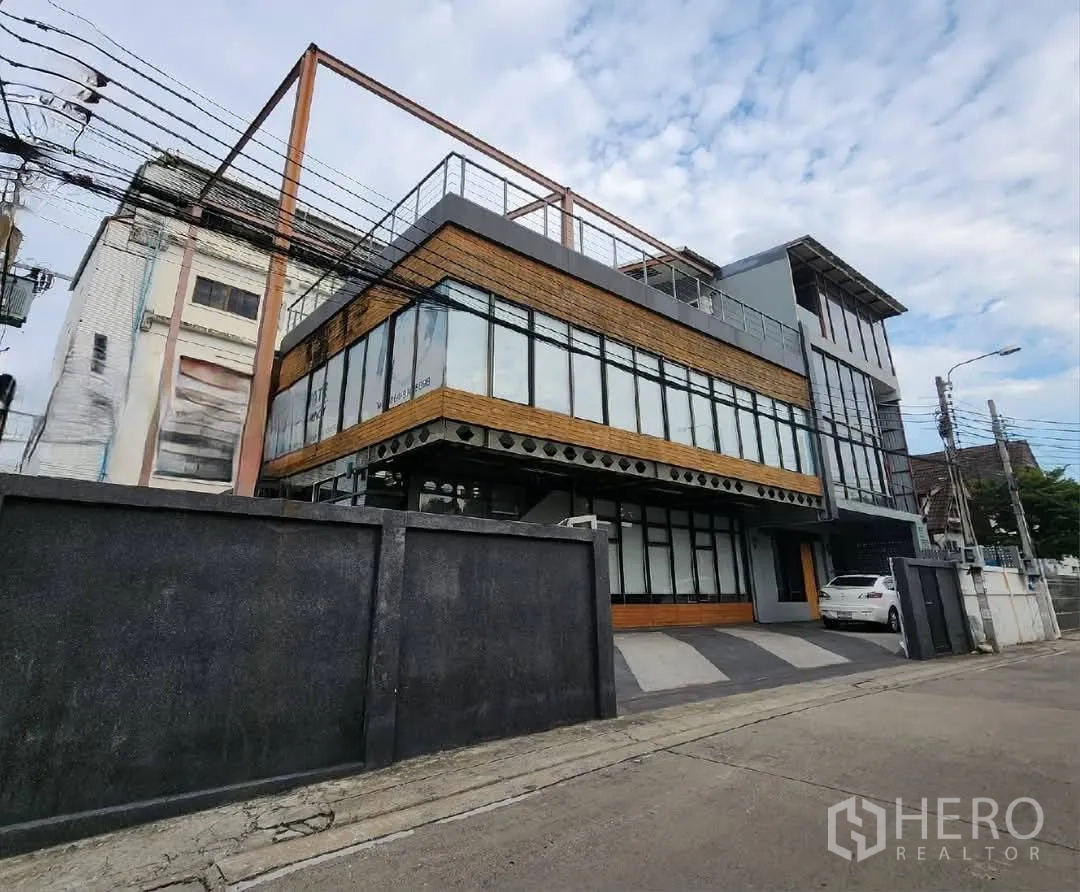 Home Office for rent in Mueang Nonthaburi, Nonthaburi - Angled exterior of the gated home office with driveway parking and wide windows.