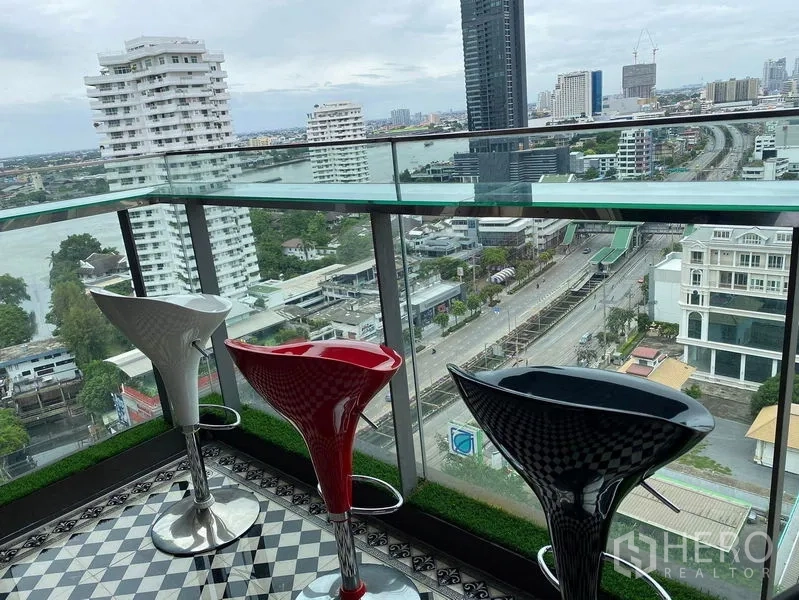 Condominium for sale in Bang Kho Laem, Bangkok - Glass-railed balcony with bar stools overlooking river and skyline.
