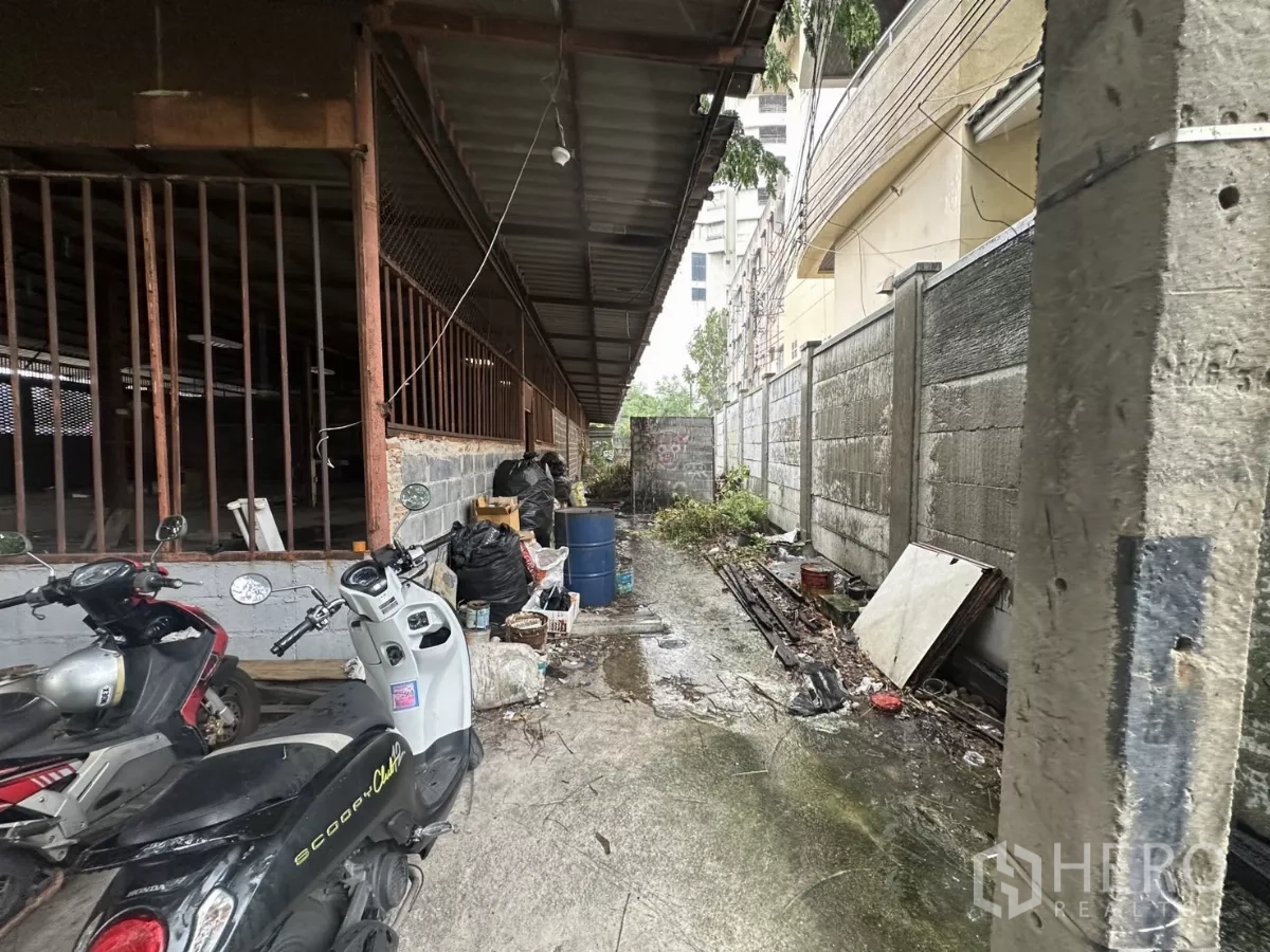 Warehouse for rent or sale in Yan Nawa, Bangkok - Side service alley along the warehouse exterior with corrugated roof, brick wall and parked motorbikes.