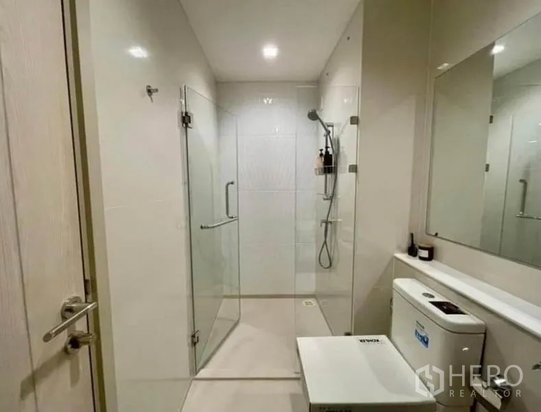 Condominium for rent in Pathum Wan, Bangkok - Clean bathroom with glass-enclosed shower, large mirror, and modern fixtures.