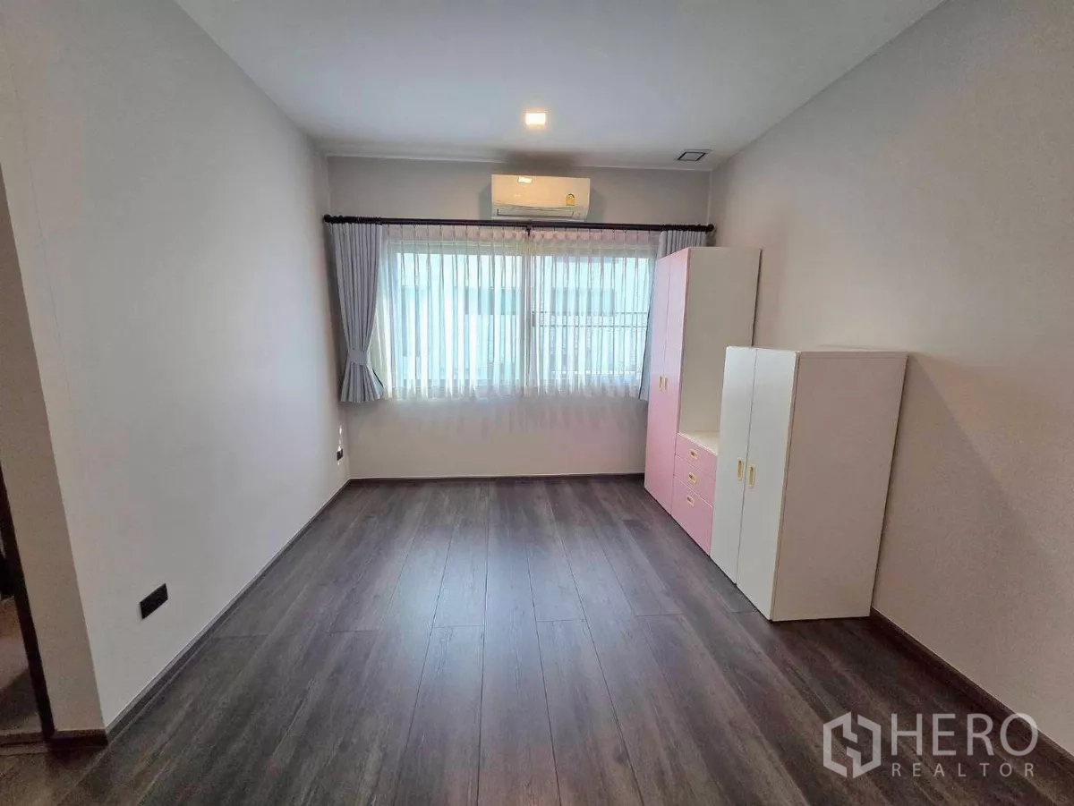 Detached House for rent in Bang Phli, Samut Prakan - Bright secondary bedroom with air-conditioner and pastel wardrobe facing a curtained window.