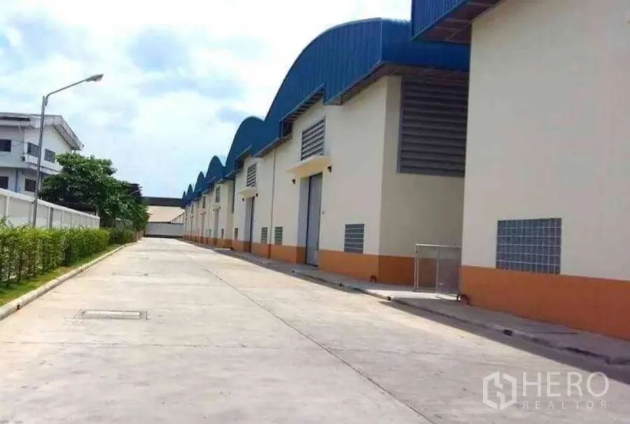 工厂 出租在Krathum Baen, Samut Sakhon - 工厂外立面与蓝色锯齿屋顶，宽阔混凝土车道适合卡车通行，位于Krathum Baen。
