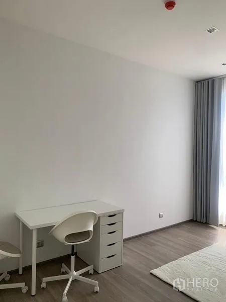 Condominium for rent in Bang Kho Laem, Bangkok - Minimalist room with desk, chair, and sheer curtains by the window.