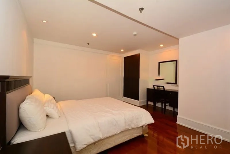 อพาร์ทเมนท์ ให้เช่าในKhlong Toei, Bangkok - ห้องนอนอบอุ่น เตียงคู่ ไฟดาวน์ไลท์ โต๊ะทำงาน และตู้เสื้อผ้าบนพื้นไม้