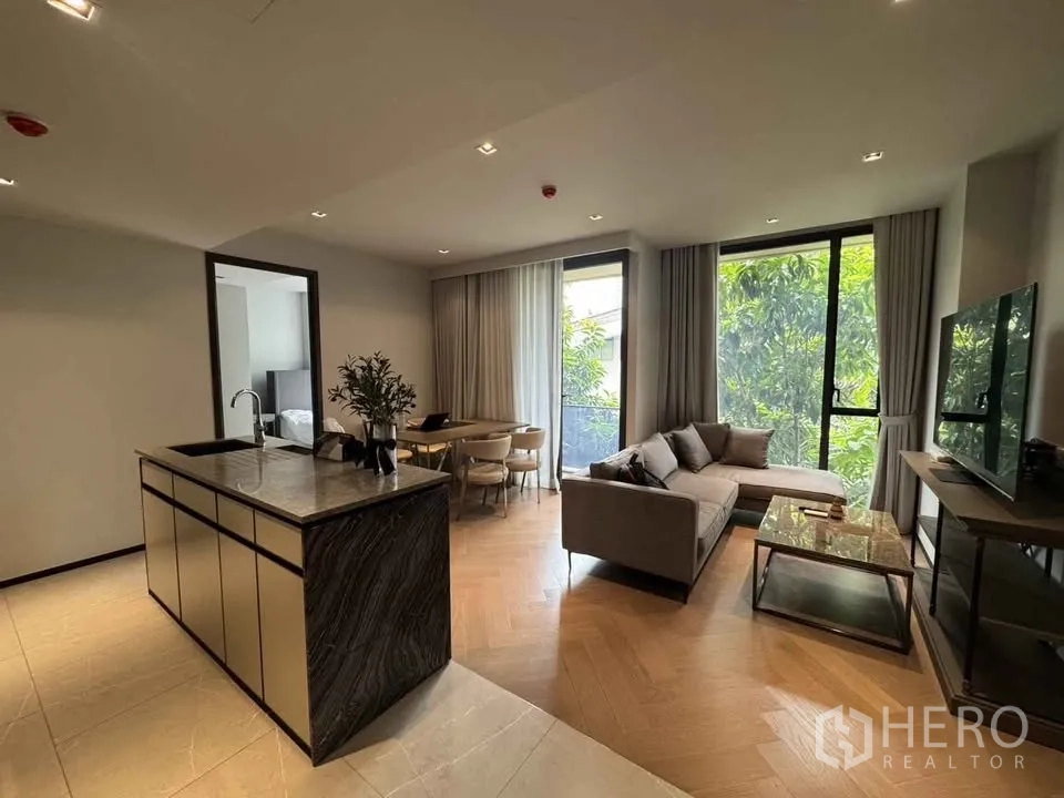 Condominium for rent in Watthana, Bangkok - Living-dining area with island, sofa, round table and tall windows to leafy view.