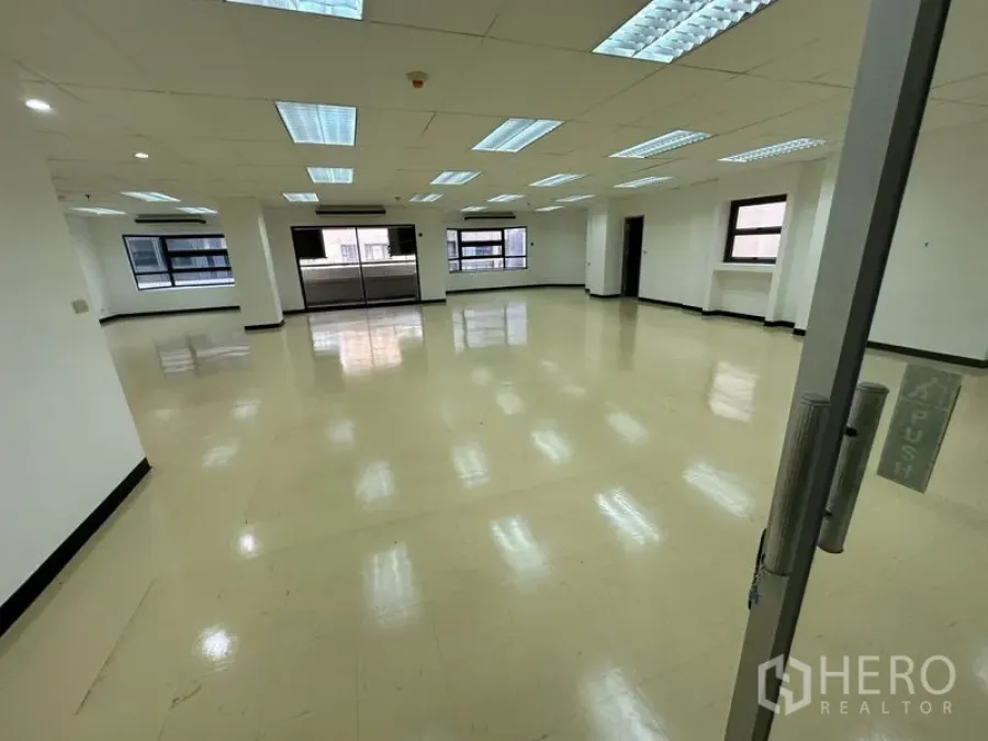 Office Space for rent in Pathum Wan, Bangkok - View from glass door entry into a spacious open-plan office with grid ceiling and windows.