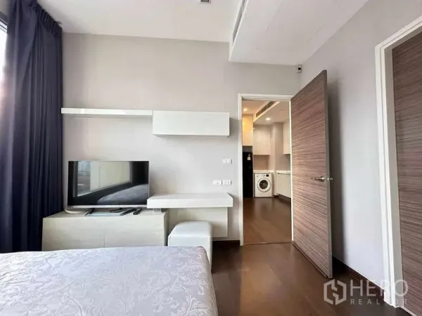 คอนโด ขายในRatchathewi, Bangkok - มุมห้องนอนมีชั้นวางทีวีและโต๊ะทำงาน มองเห็นทางเข้าครัวและเครื่องซักผ้า