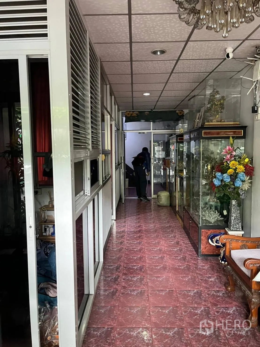 Shophouse for rent in Khlong Toei, Bangkok - Long interior hallway with glass cases and seating along red tiled floors.