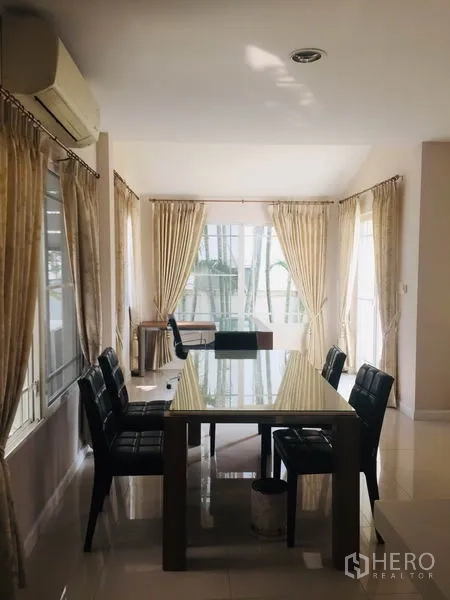 Detached House for rent in Bang Kapi, Bangkok - Dining room with glass-top table, air conditioner and wraparound windows bringing natural light.