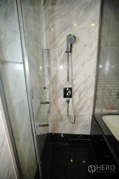 公寓 出租在Bang Rak, Bangkok - 近景：大理石淋浴间，手持花洒与玻璃门。