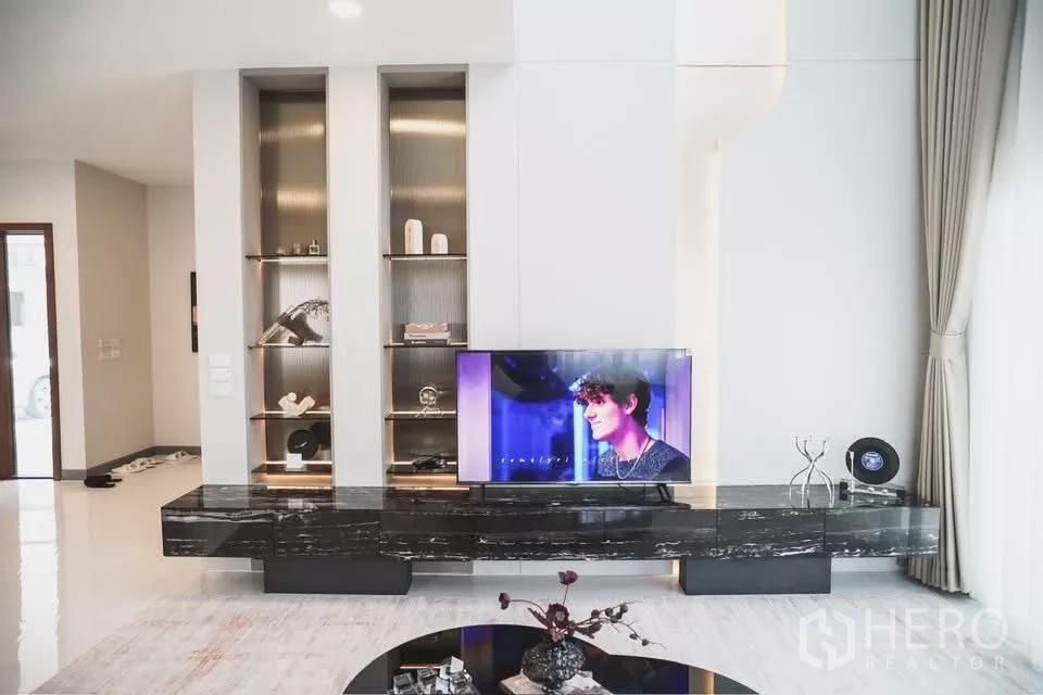 Detached House for rent in Bang Phli, Samut Prakan - Stylish living room with marble TV console, illuminated built-in shelves and full-height curtains.